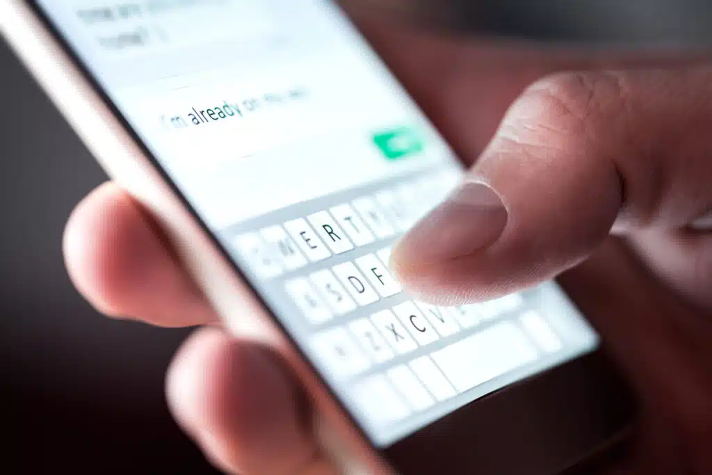 Man sending text message and sms with smartphone. Guy texting and using mobile phone late at night in dark. Communication or sexting concept. Finger typing with cellphone keyboard.